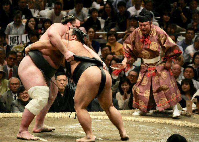 Two sumo wrestlers grappling in a sumo ring as a crowd watches.